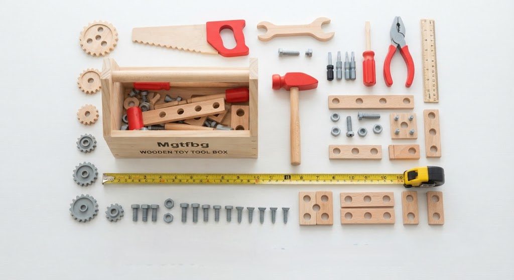 Mgtfbg 29-piece wooden tool set actual size comparison with measuring tape and standard toy hammer, all pieces neatly arranged including gears nuts screws and assembly parts